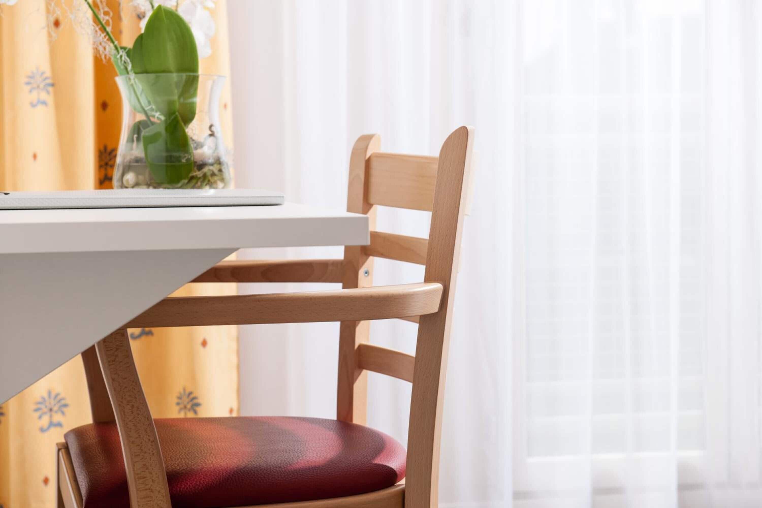 A wooden chair with a red cushion at a white table.
