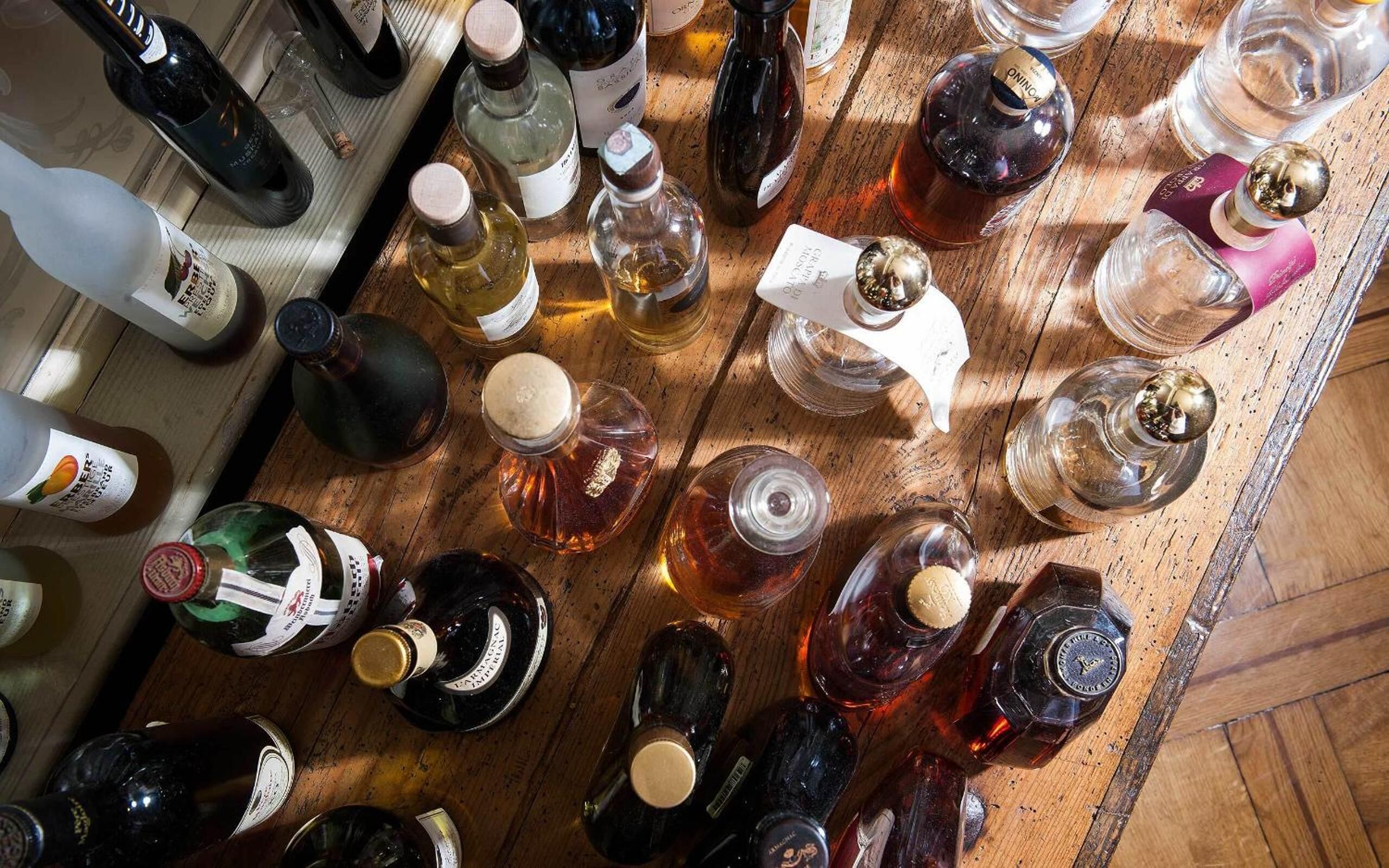 On peut voir une variété de bouteilles et de verres sur une surface en bois, probablement dans un bar ou un espace dédié à la dégustation.