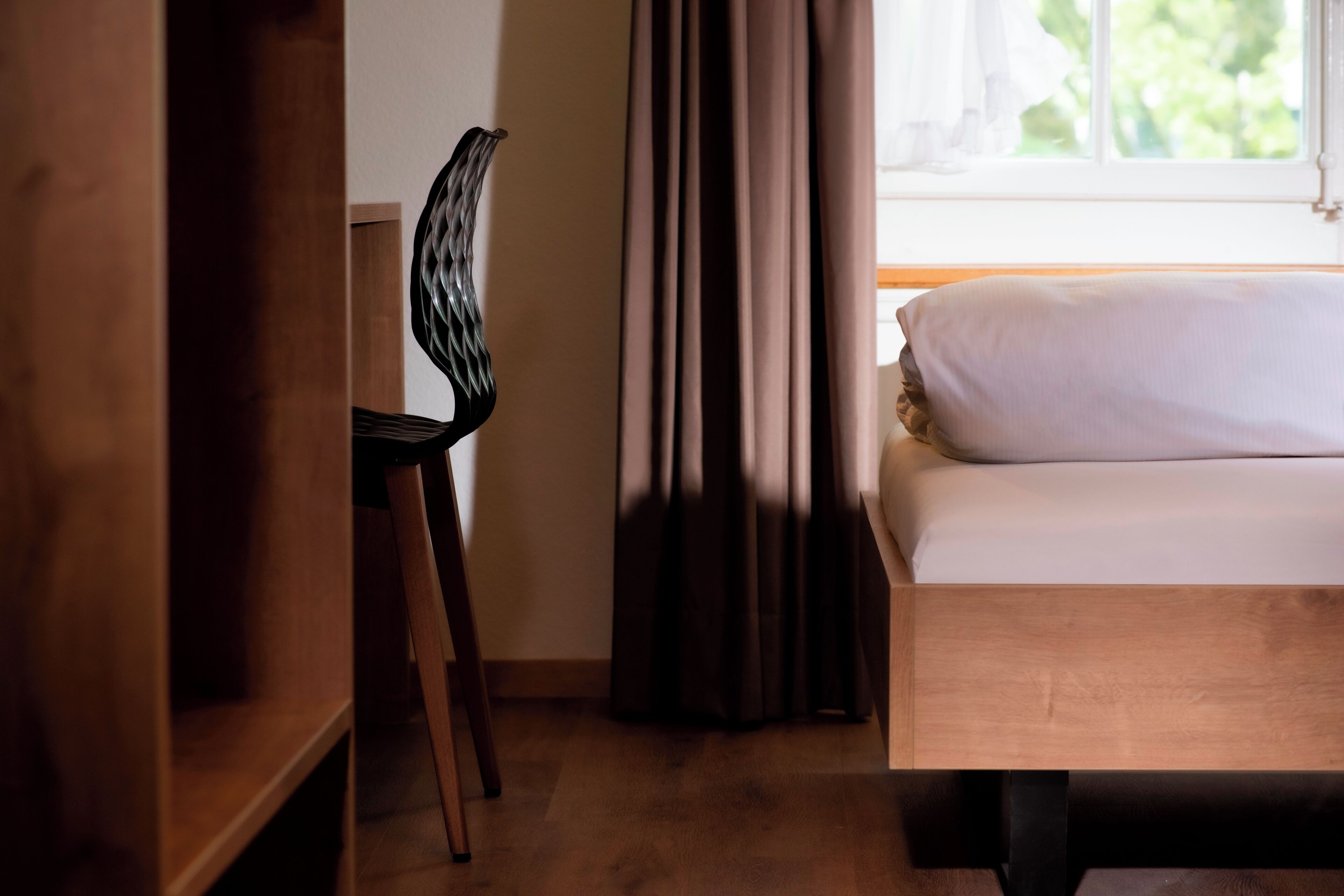 A bedroom with a wooden bed, a chair, and a window with curtains.