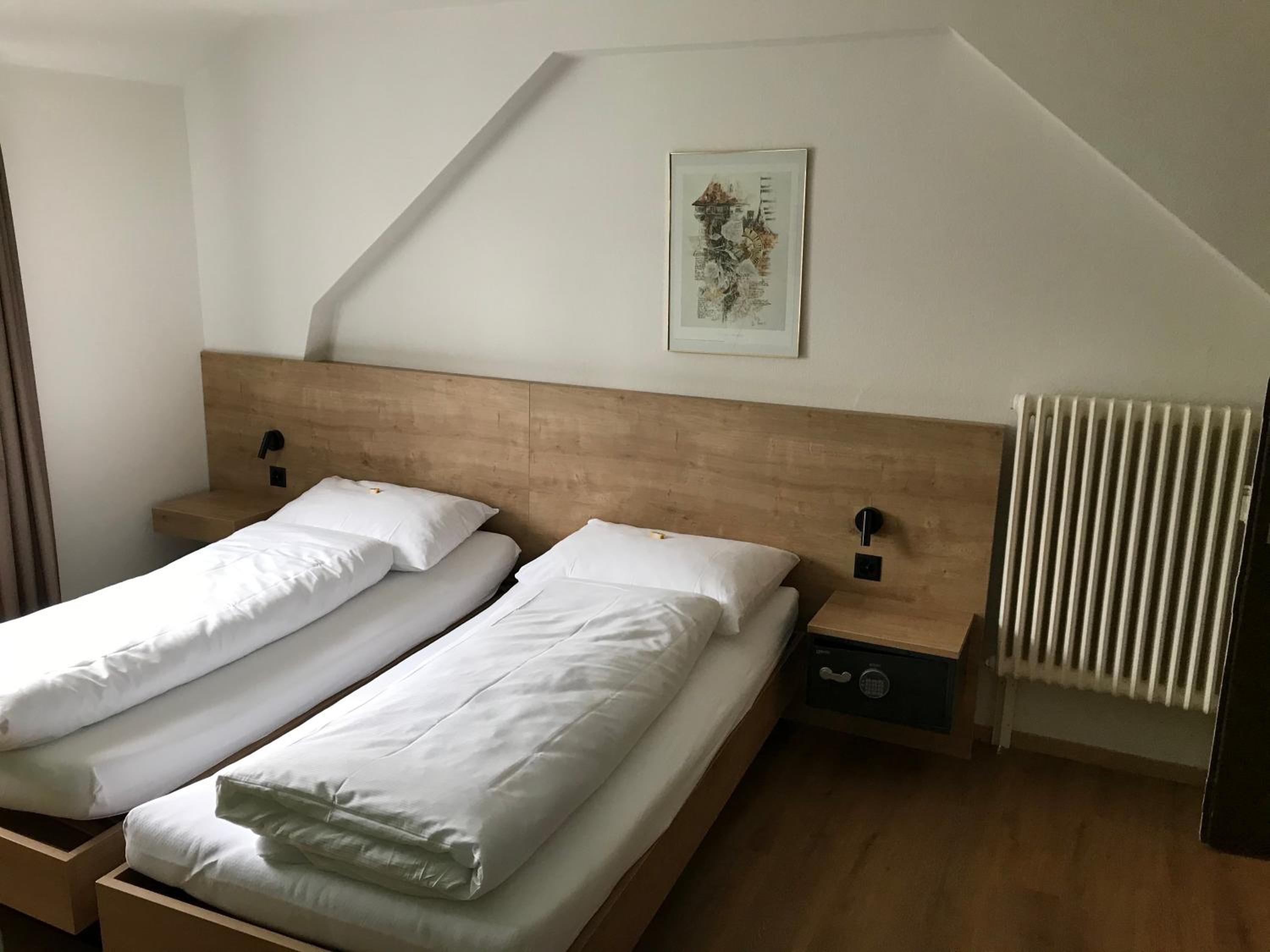 Une chambre avec deux lits simples, des têtes de lit en bois, des tables de chevet, un radiateur et un tableau encadré au mur.