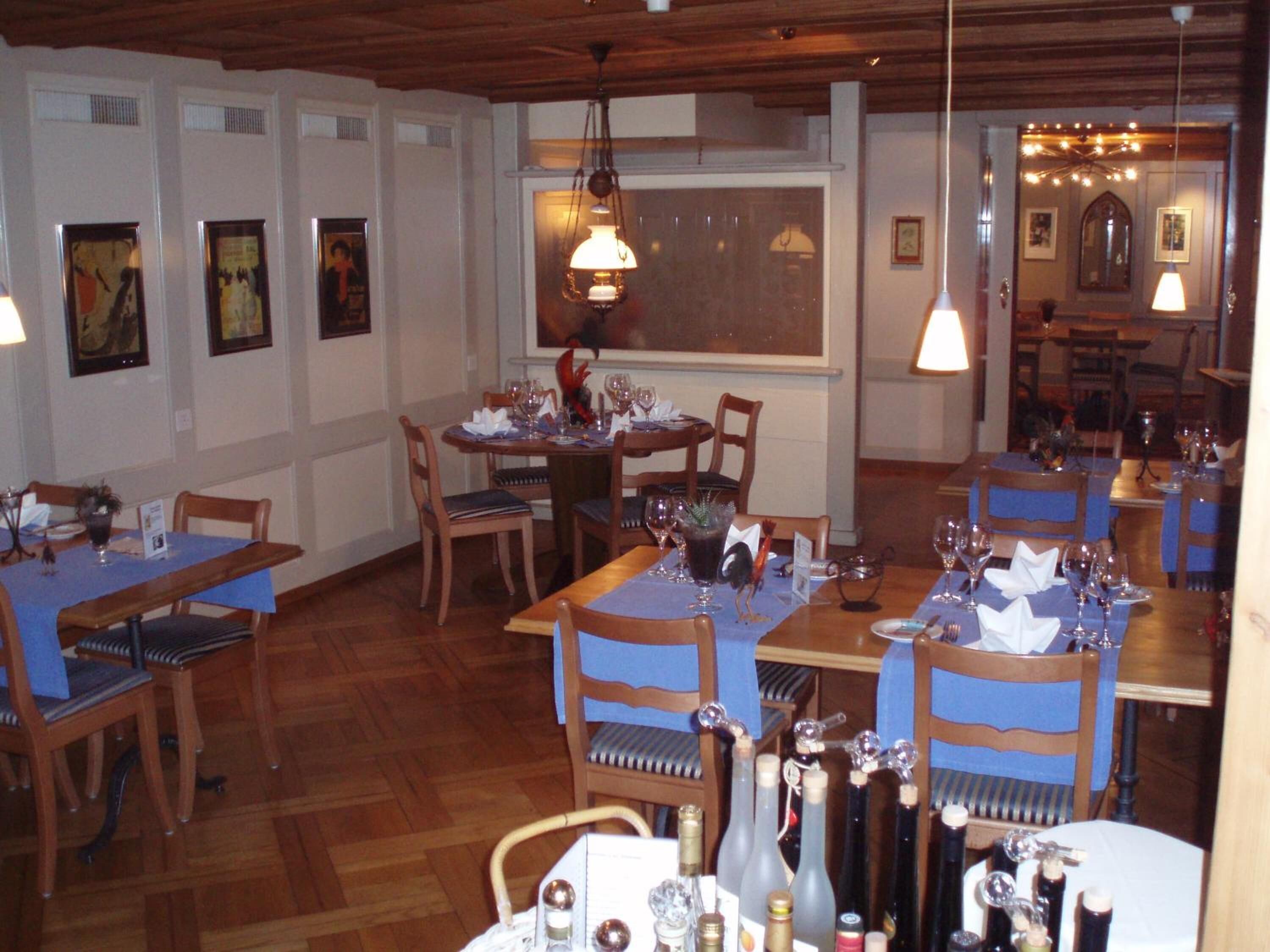 A dining area with wooden tables and chairs, a chandelier, and framed artwork on the walls.