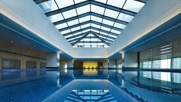 Una amplia piscina interior con techo de vidrio y reflejo en el suelo.