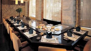 Una larga mesa de comedor comunal con múltiples platos de comida, ubicada en un restaurante moderno con paredes de piedra y vigas de madera en el techo.