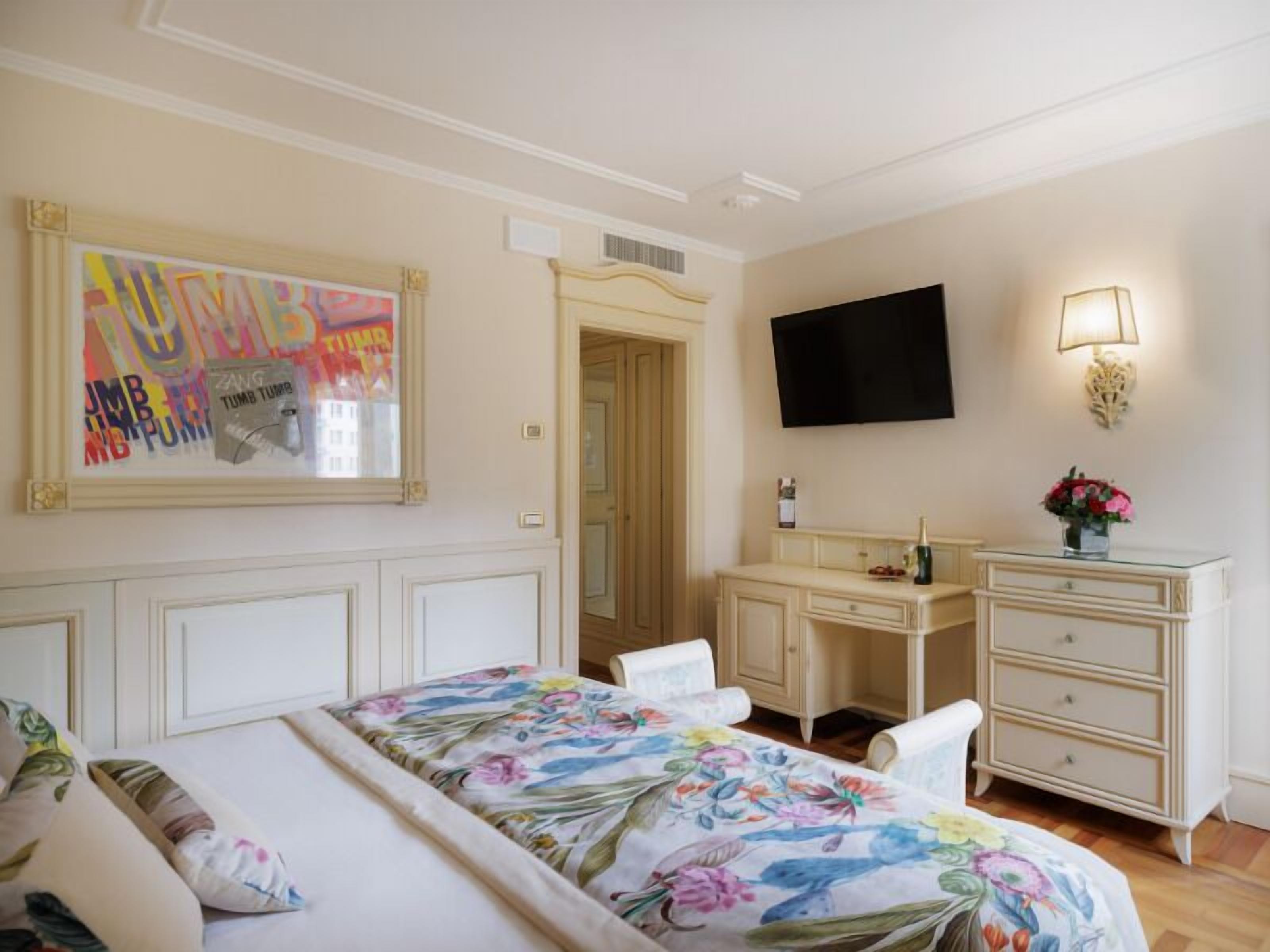 Un dormitorio con cama, escritorio, silla, televisor y lámpara de pared.