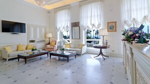 Un vaste salon doté d’un haut plafond, de lustres élégants et de grandes fenêtres ornées de rideaux blancs.