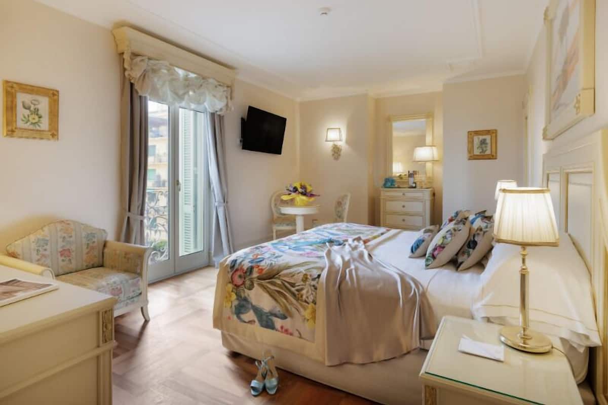 Ein Hotelzimmer mit Bett, Schreibtisch, Stuhl, Fernseher, Lampe und einem Fenster mit Vorhängen.
