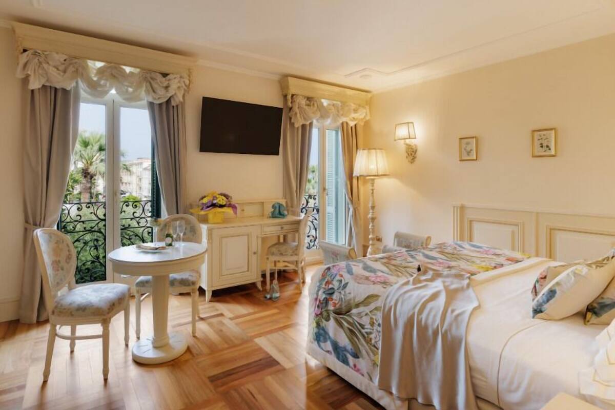 Ein Hotelzimmer mit Bett, Schreibtisch, Stuhl, Fernseher und einem Balkon mit Vorhängen.