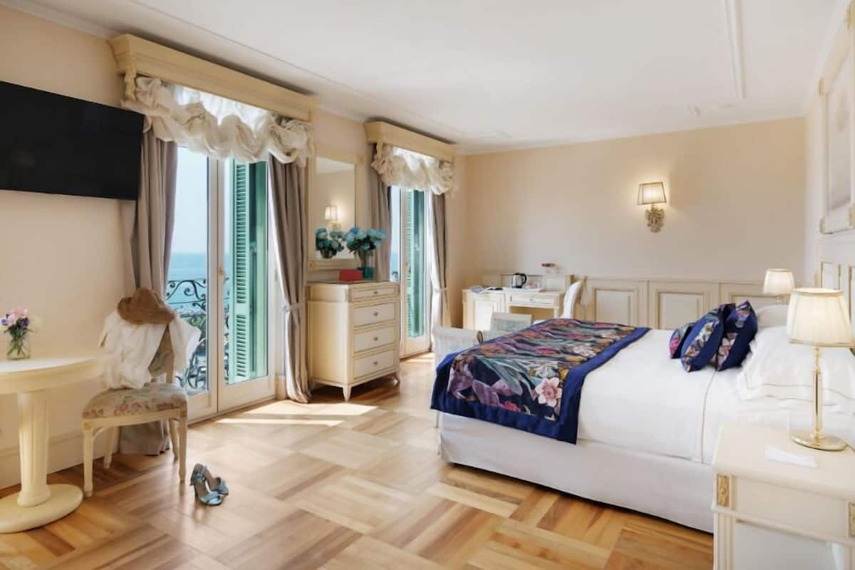 Ein Hotelzimmer mit Bett, Schreibtisch, Stuhl, Schminktisch mit Spiegel und Wand-Fernseher.