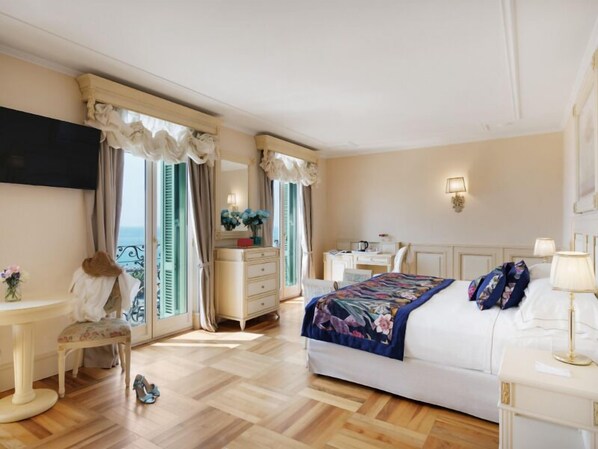 A hotel room with a bed, a desk, a chair, a vanity with a mirror, and a television mounted on the wall.