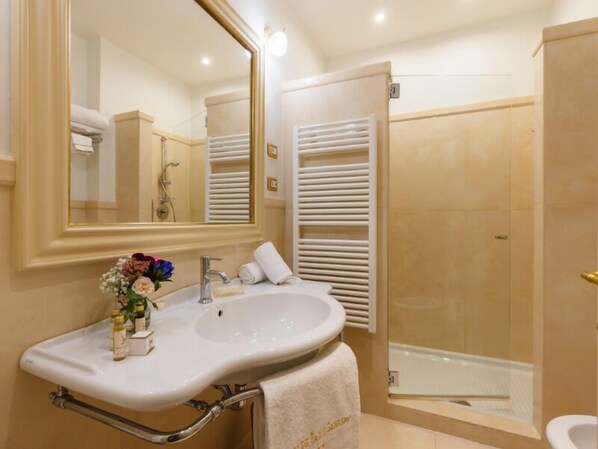 Un baño con un espejo grande, un lavabo con una toalla y zona de ducha.