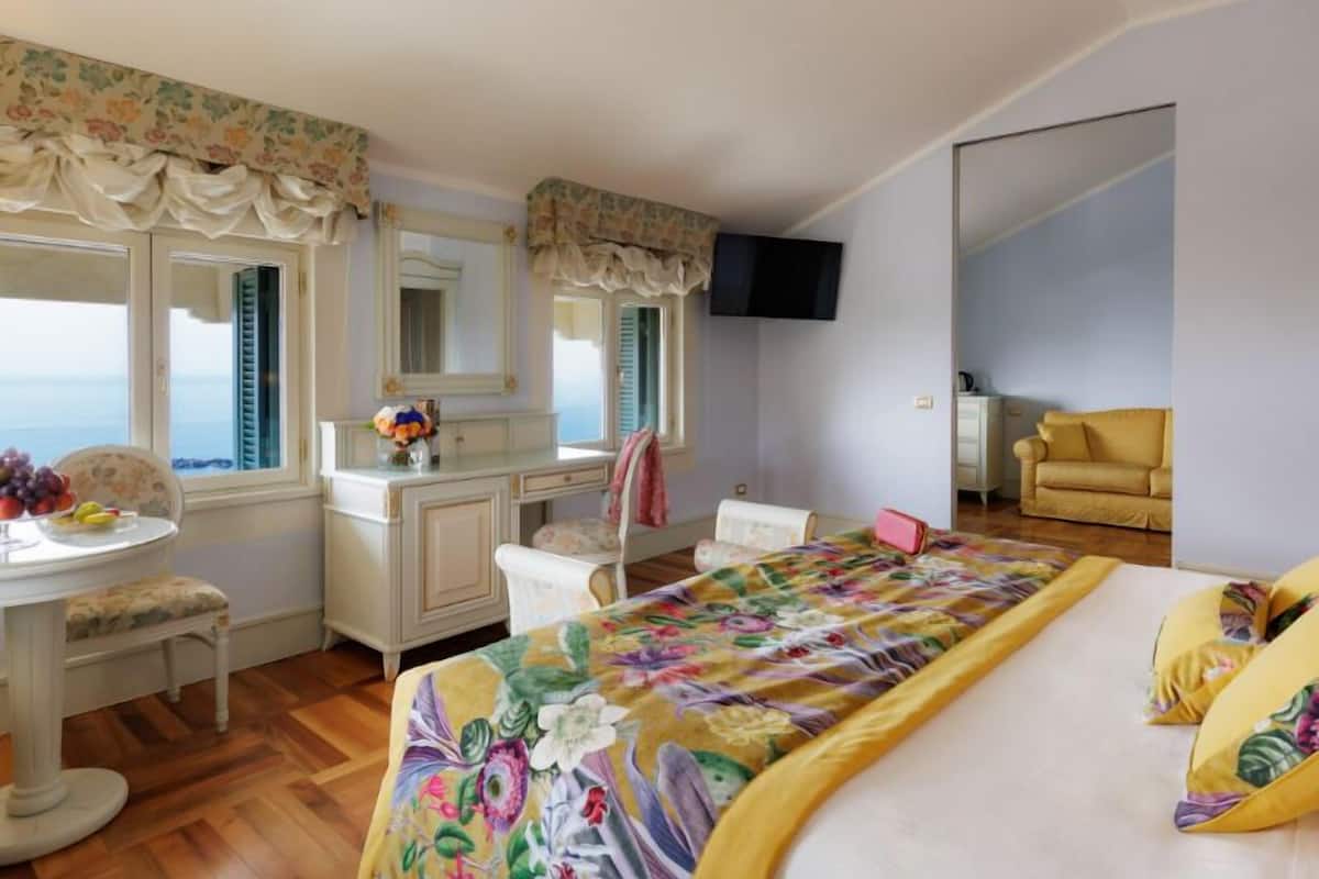 Ein Schlafzimmer mit Bett, Schreibtisch, Stuhl, Fernseher und Meerblick.