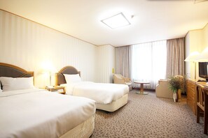 Quarto de hotel com duas camas, uma escrivaninha, uma cadeira, uma mesinha e uma televisão.