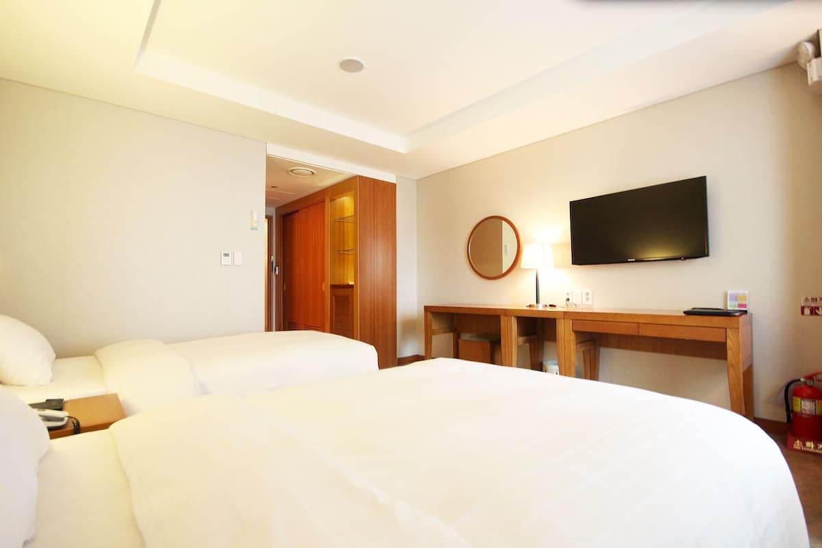 A hotel room with two beds, a desk with a flat-screen TV, a mirror, and a fire extinguisher.