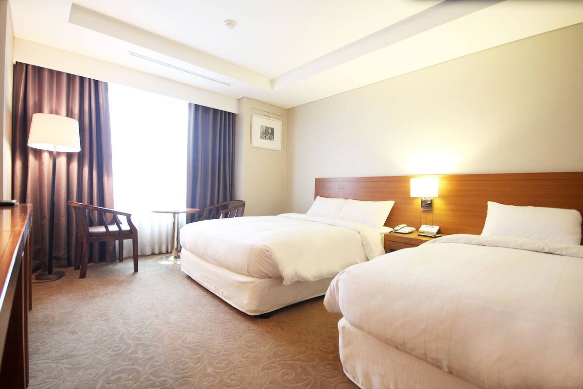 A hotel room with two beds, a desk, a chair, a lamp, and a picture on the wall.