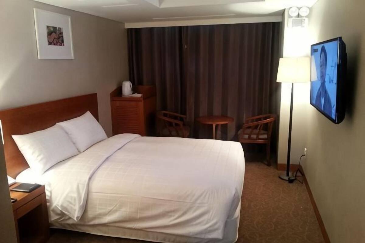 A hotel room with a large bed, a desk, a chair, a TV, and a window with curtains.
