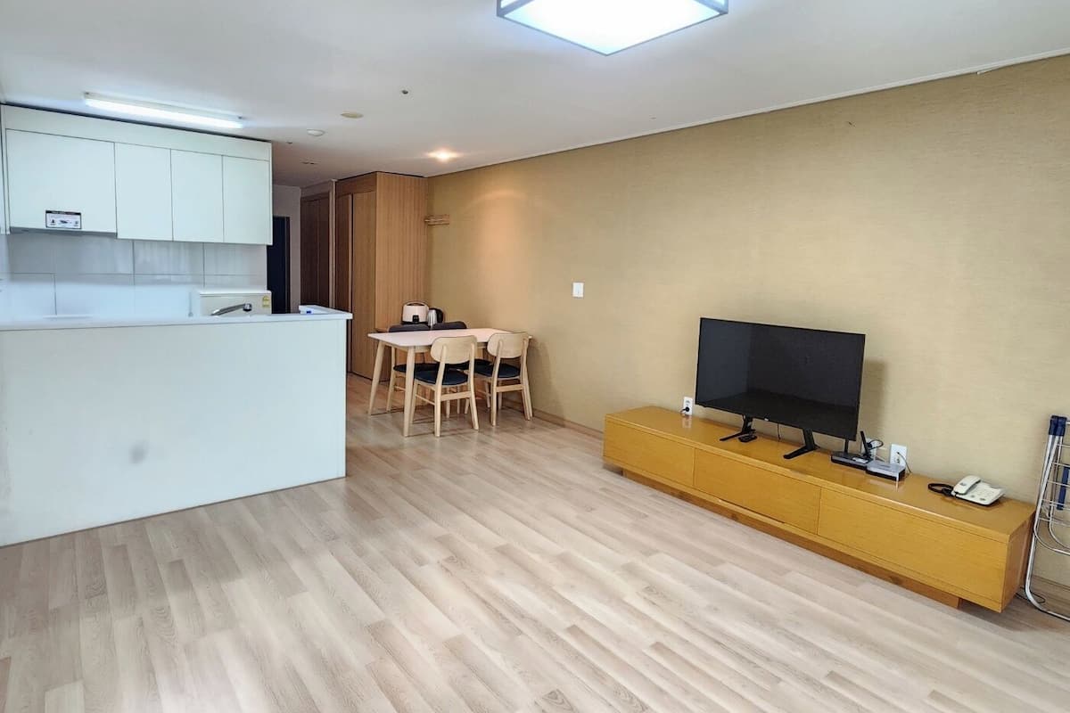 A modern living space with a kitchen, dining area, and a TV on a wooden console.