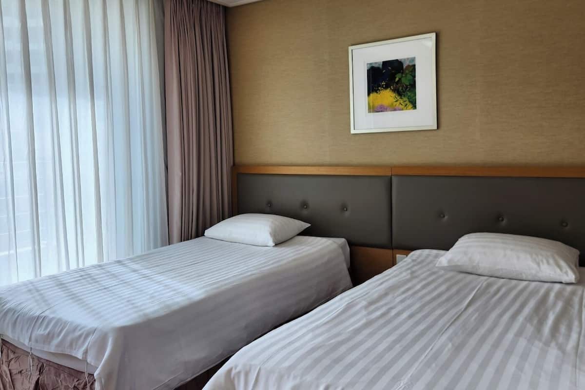 A hotel room with two beds, a large window with curtains, a framed picture on the wall, and a neutral-colored headboard.