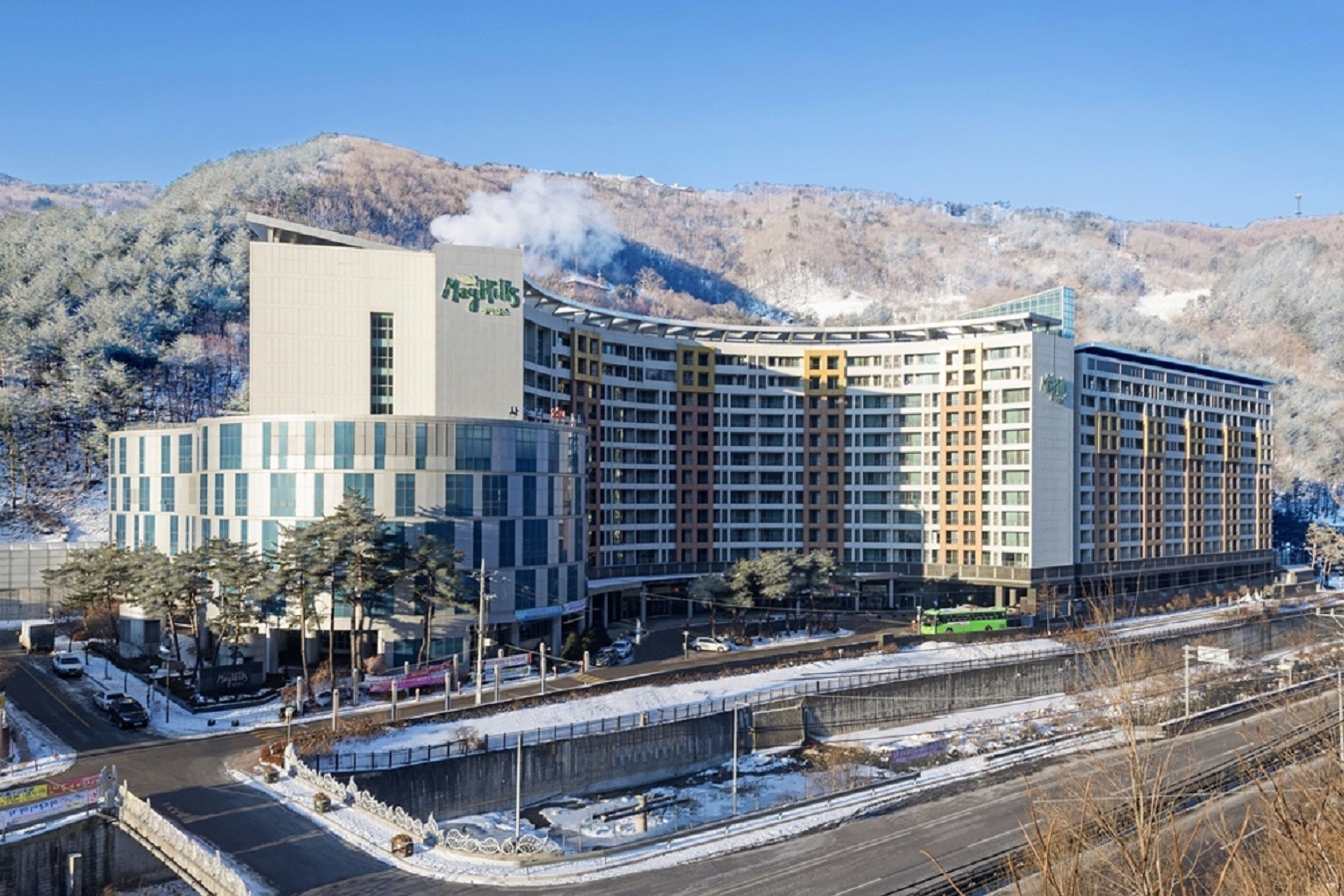 A large hotel with multiple floors and a curved facade, situated near a railway track with snow on the ground.