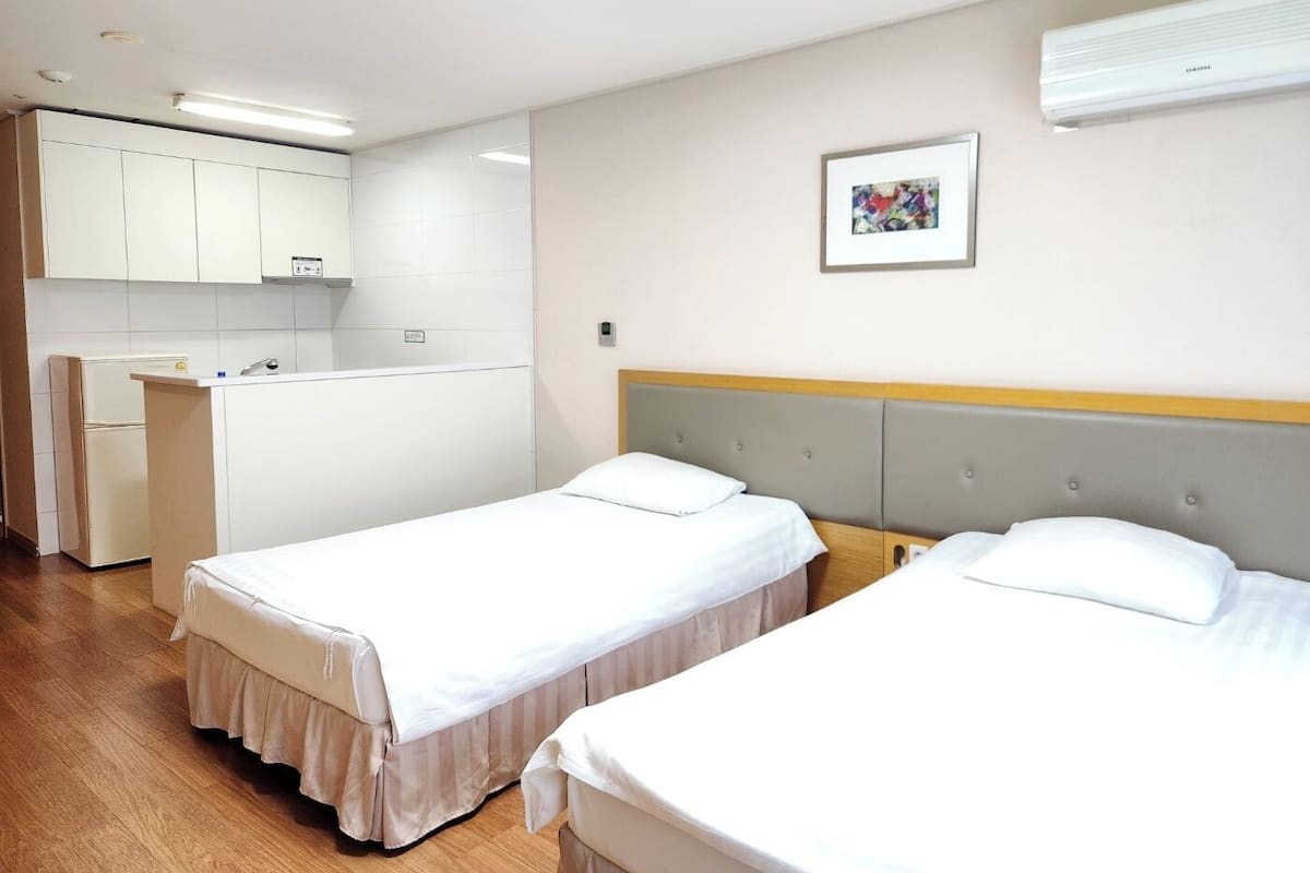 A hotel room with two beds, a kitchenette, and a bathroom.