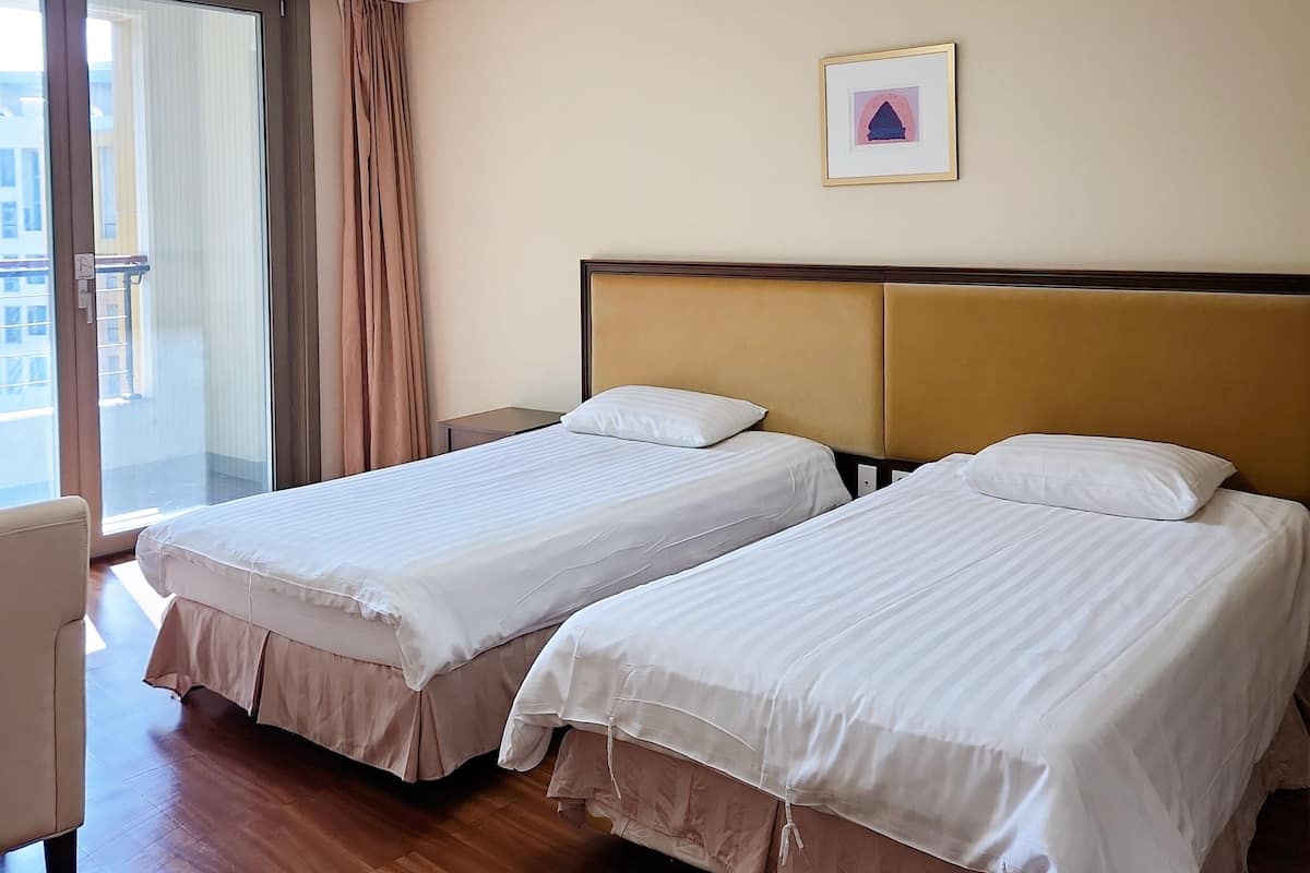 A hotel room with two beds, a large window, and a framed picture on the wall.