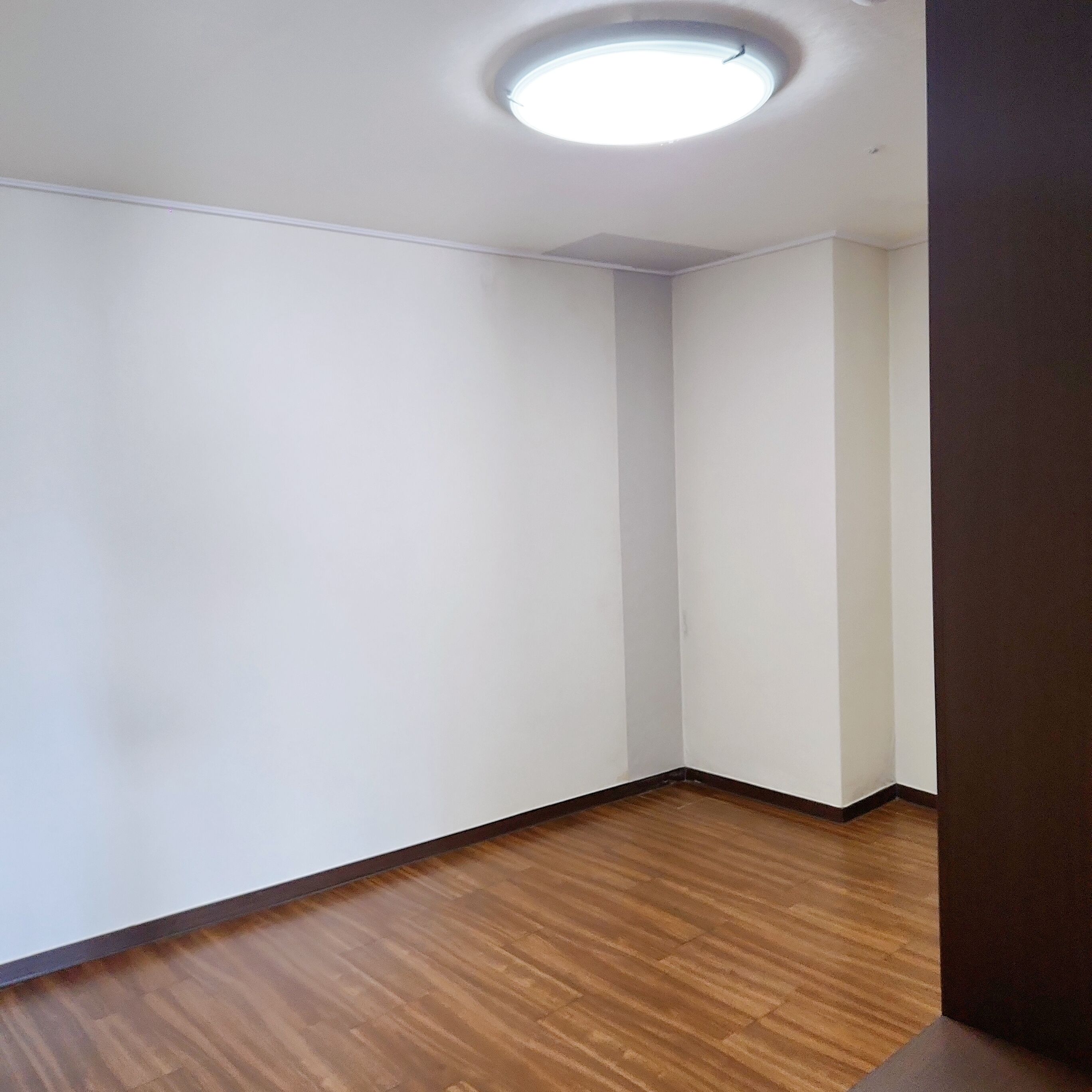 A corner room with white walls, a wooden floor, and a ceiling light.