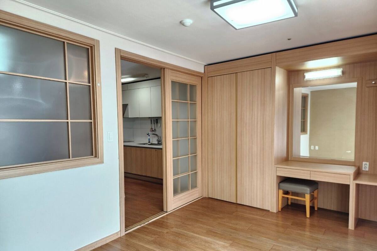 A modern room with a wooden floor, a built-in wardrobe with sliding doors, a small stool, and a mirror above a vanity.