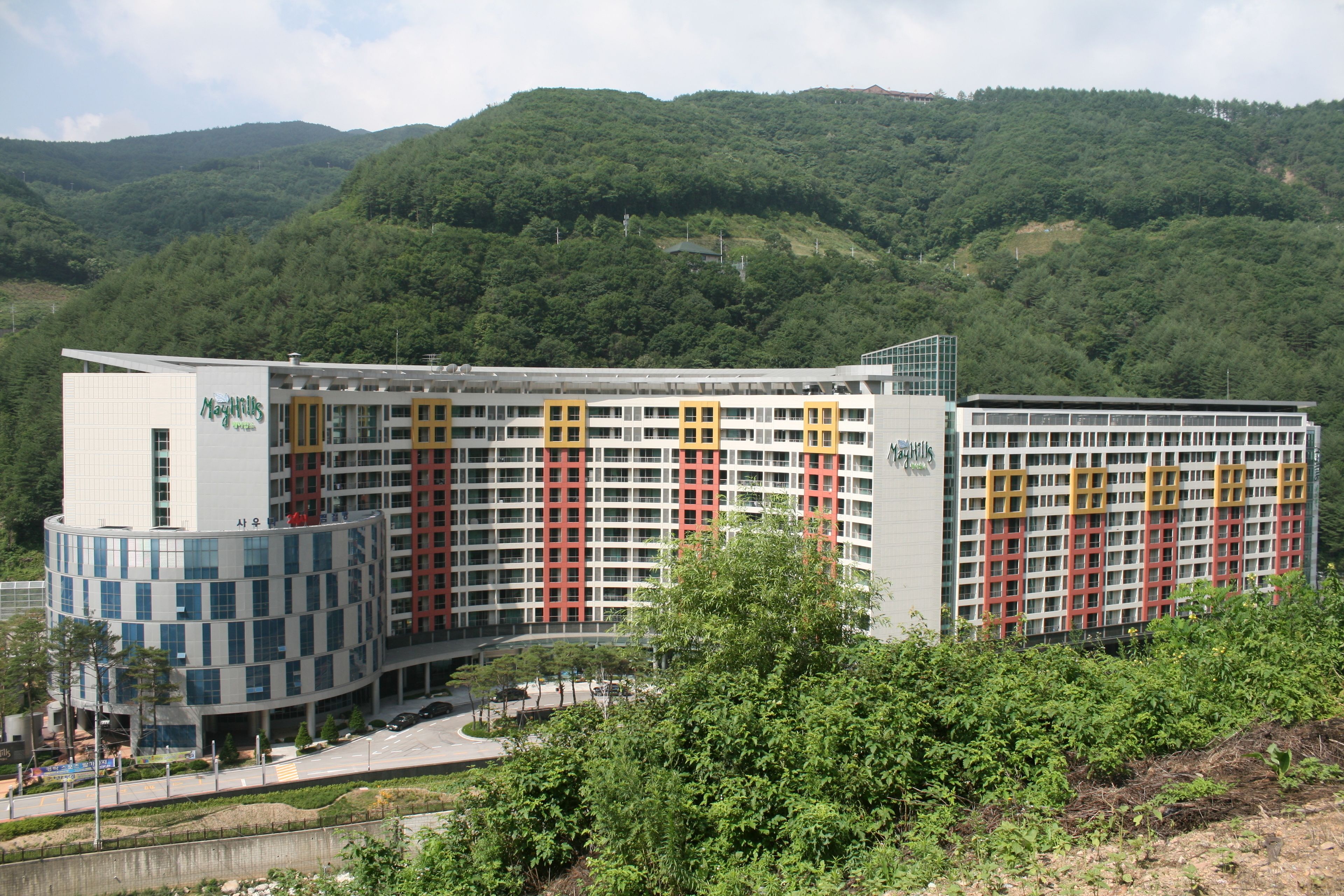 A modern hotel with multiple floors, a central courtyard, and a view of a green hill.