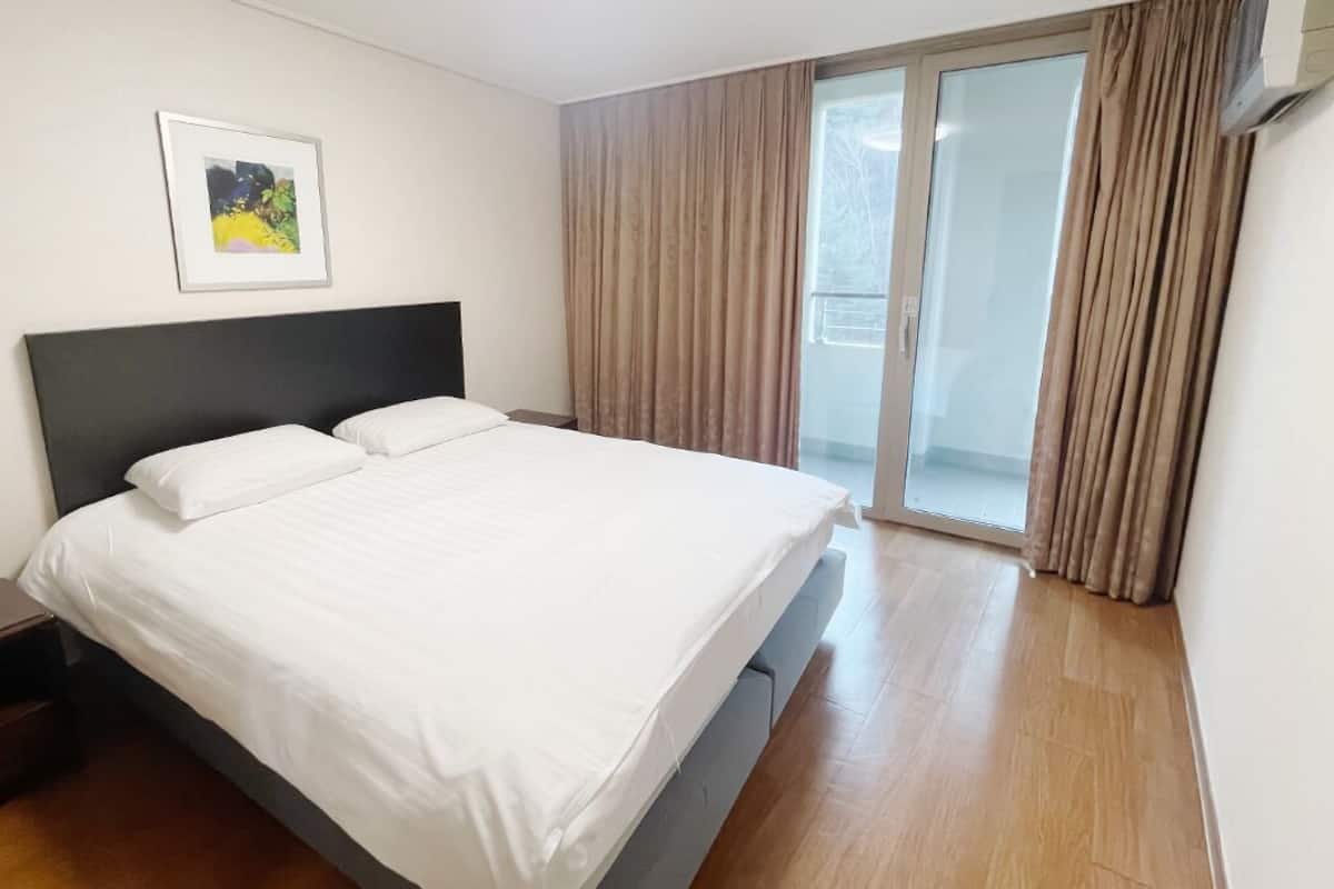 A hotel room with a bed, a nightstand, a framed picture on the wall, and a sliding glass door leading to a balcony.