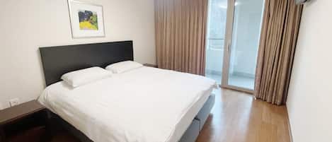 A hotel room with a bed, a nightstand, a framed picture on the wall, and a sliding glass door leading to a balcony.