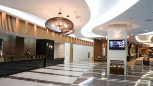 A spacious lobby with a high ceiling, a large chandelier, a reception desk, and a television screen. - Mayhills Resort (Jeongseon)
