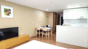 Una sala de estar moderna con televisor de pantalla plana, un comedor con mesa y sillas, y una kitchenette con armarios blancos.
