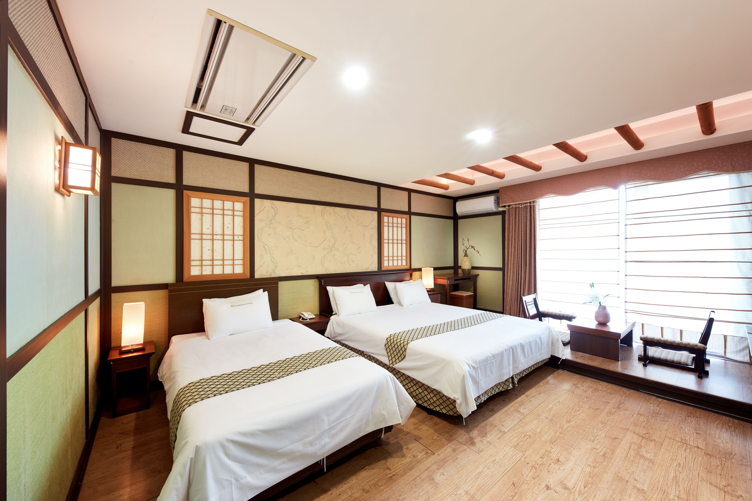 A hotel room with two beds, a wooden floor, a map on the wall, and a window with curtains.