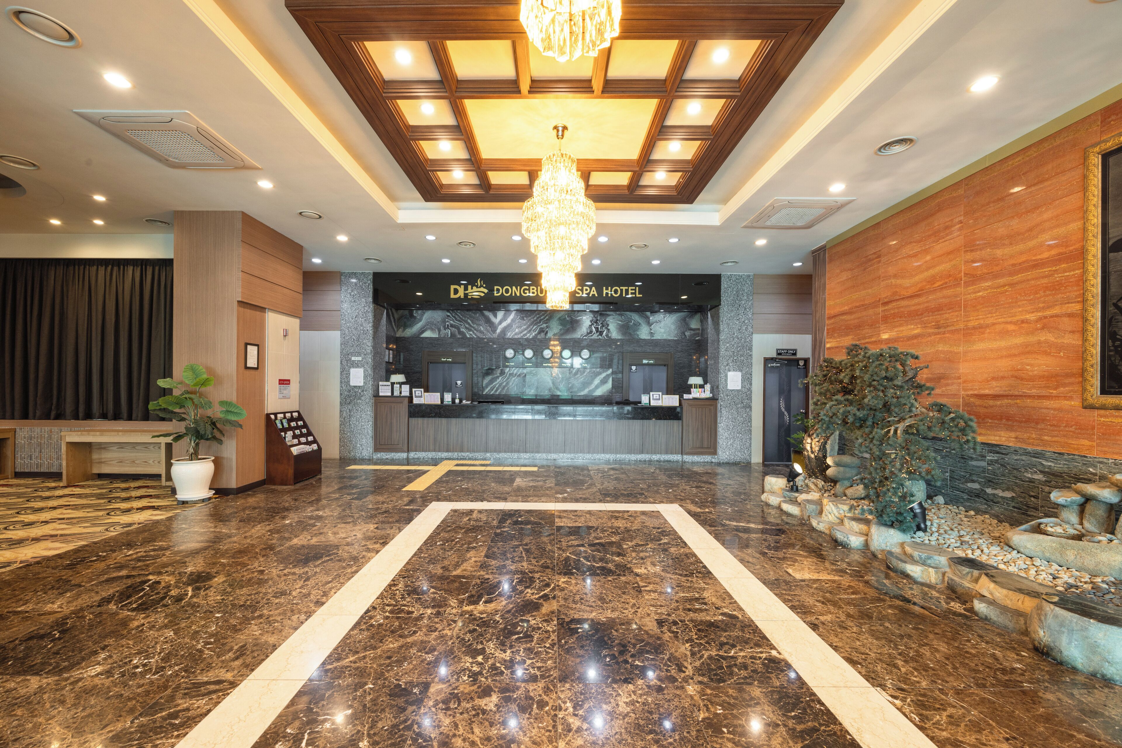 A hotel lobby with a reception desk, a chandelier, marble flooring, and a reception counter.