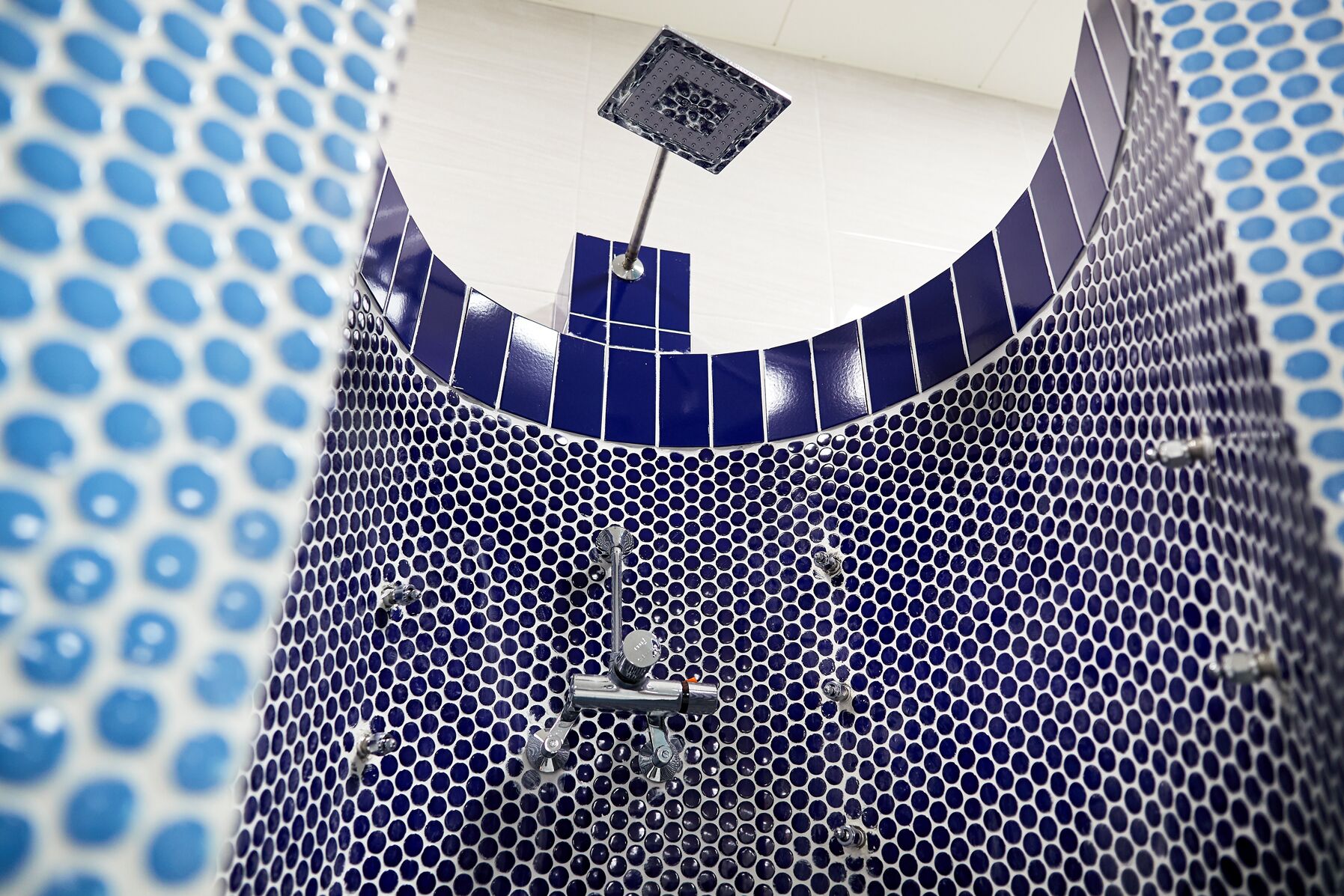 Une salle de bain avec un mur recouvert de carreaux bleus et blancs, une pomme de douche et un panneau de commande.