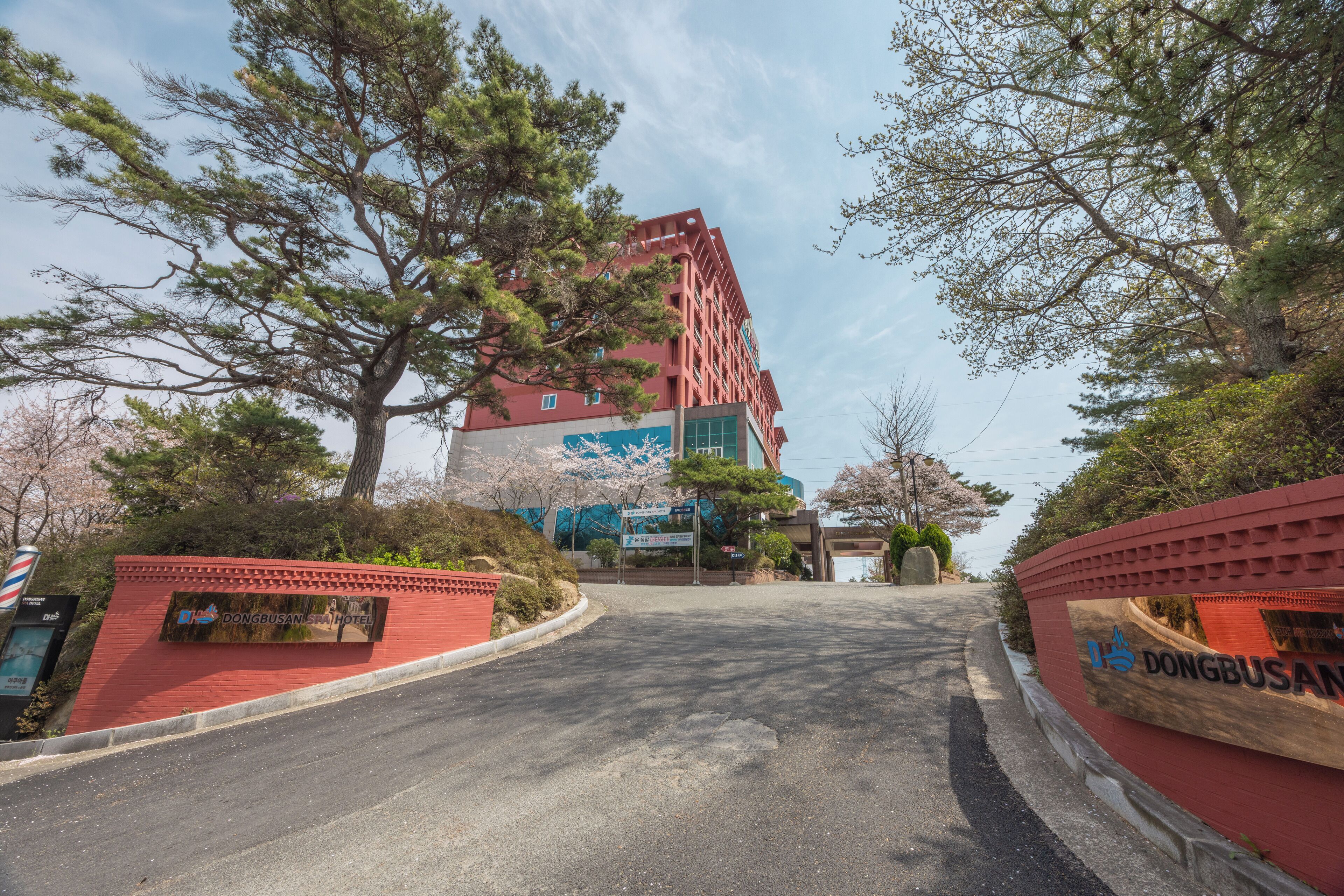 A hotel entrance with a red brick facade, a large tree in the foreground, and a clear sky.
