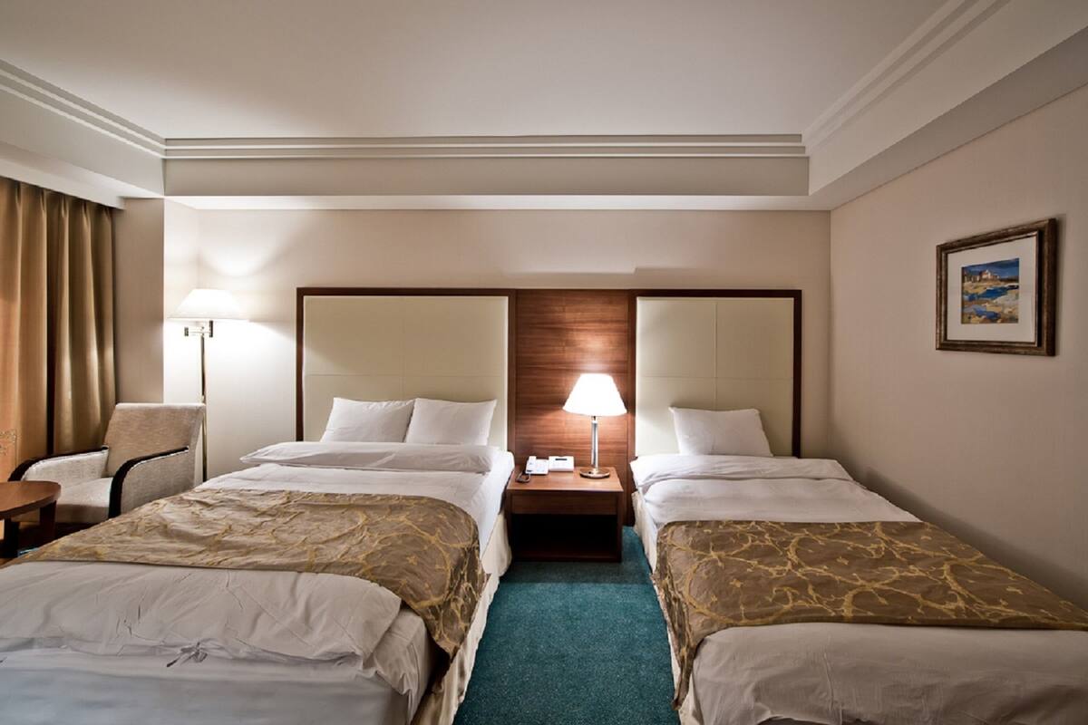 Ein Hotelzimmer mit zwei Betten, einem Schreibtisch, einem Stuhl, einer Lampe und einem Bild an der Wand.
