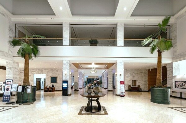 A spacious lobby with a high ceiling, marble flooring, and a central round table with vases.