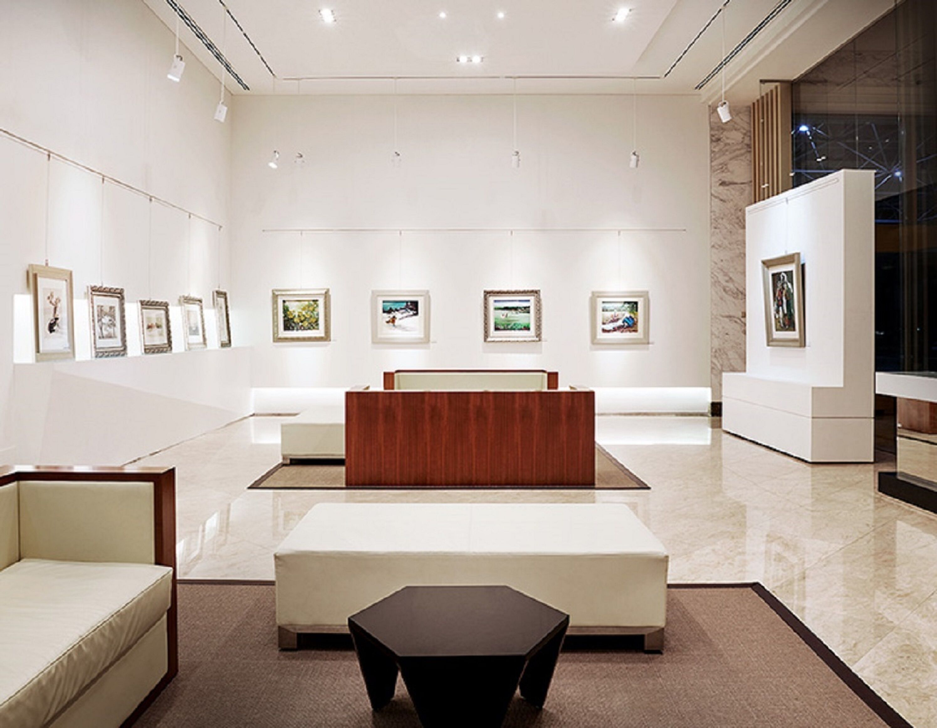 A modern art gallery with a reception desk, white sofas, and framed artworks on the walls.