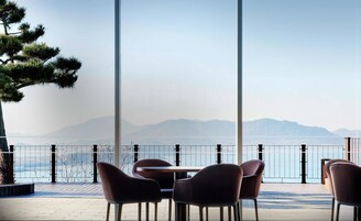 Terraza con sillas y una mesa con vista a un cuerpo de agua y montañas lejanas.