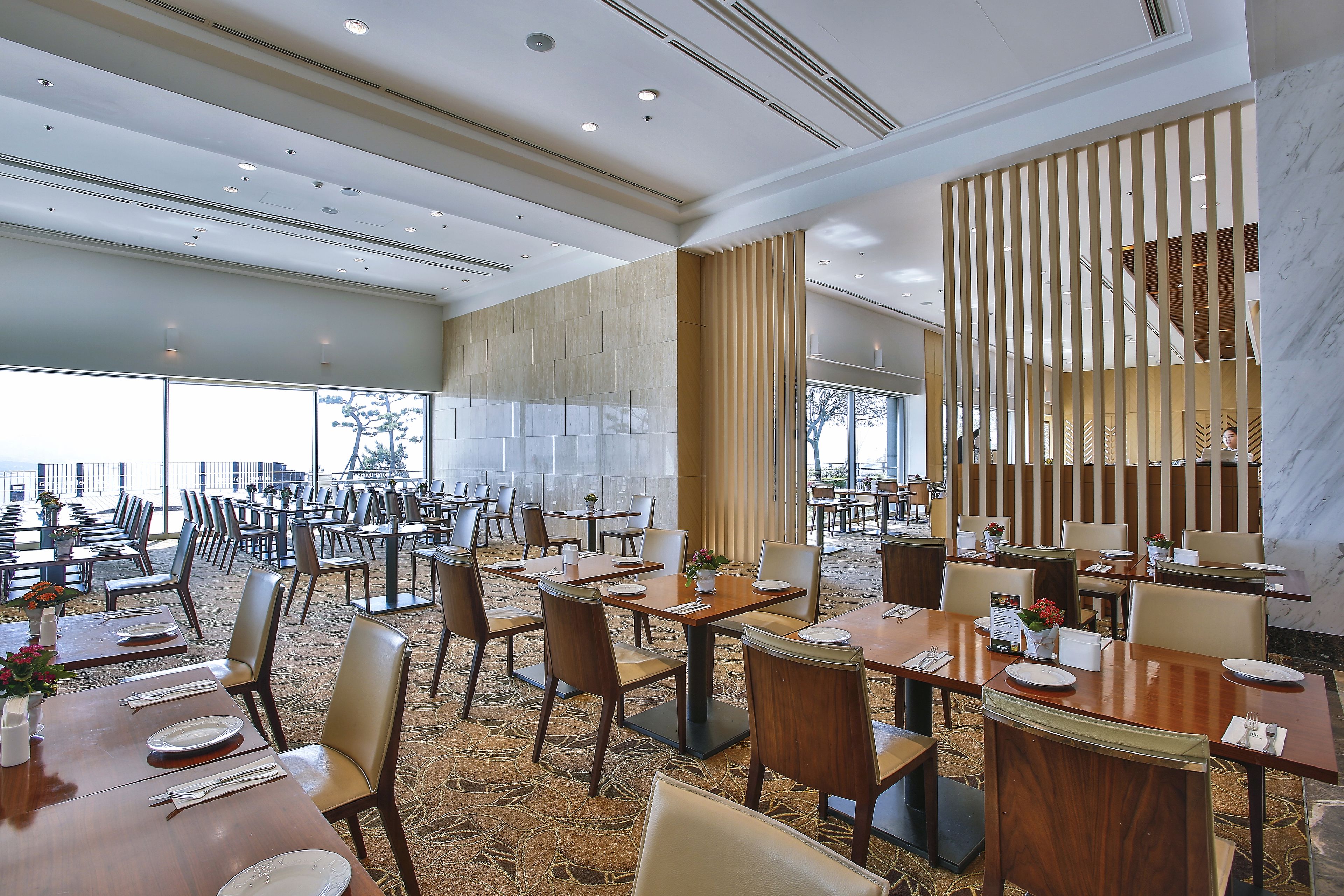 Un'ampia sala da pranzo con diversi tavoli e sedie, un pilastro in marmo e vista sull'esterno.
