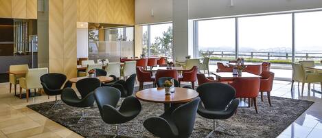 A modern dining area with round tables and black chairs, large windows with a view, and a mix of red and yellow chairs.