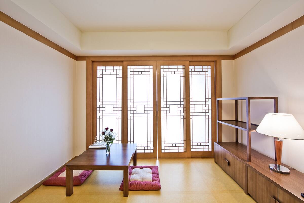 Ein Zimmer mit einem Holztisch, einer Couch, einer Lampe und einem TV-Schrank.
