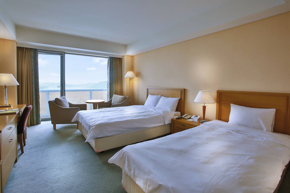 Ein Hotelzimmer mit zwei Betten, einem Schreibtisch, einem Stuhl und Meerblick.