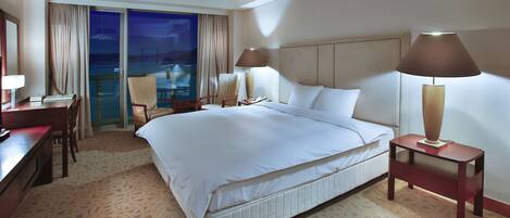 A hotel room with a large bed, two bedside tables with lamps, a desk, and a chair.
