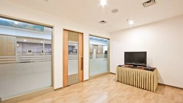 A spacious room with a large window, a television on a table, and a door leading to another room.