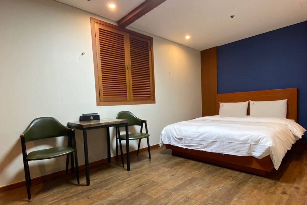 A bedroom with a bed, two chairs, a small table, and a window with wooden shutters.