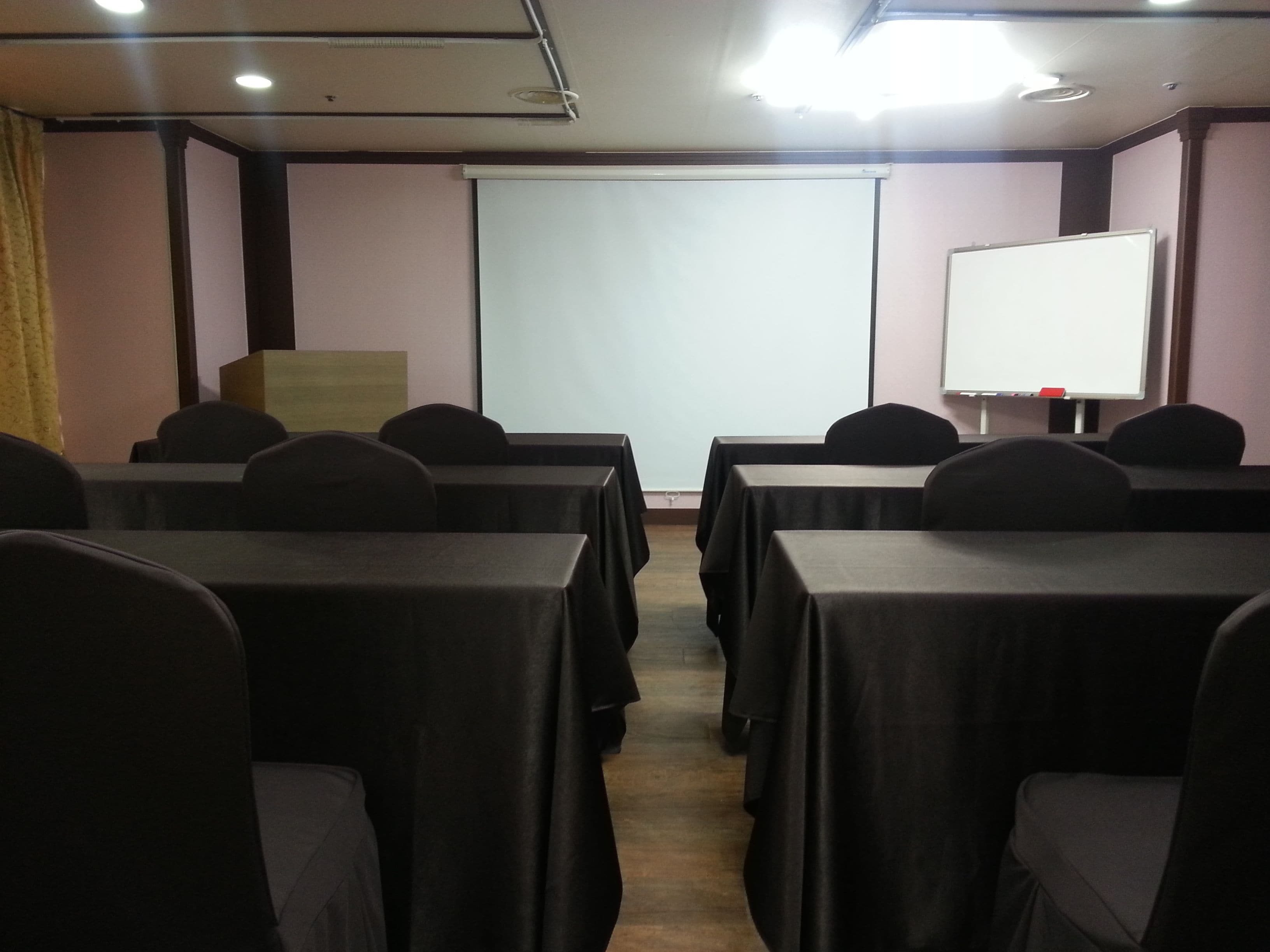 A conference room with tables and chairs, a projector screen, and a whiteboard.