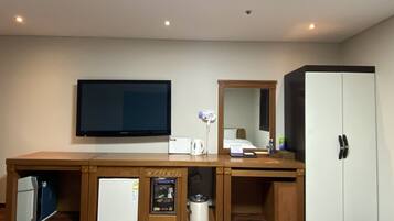 A hotel room with a large flat-screen TV, a minibar, a refrigerator, a trash can, a mirror, and a wardrobe.