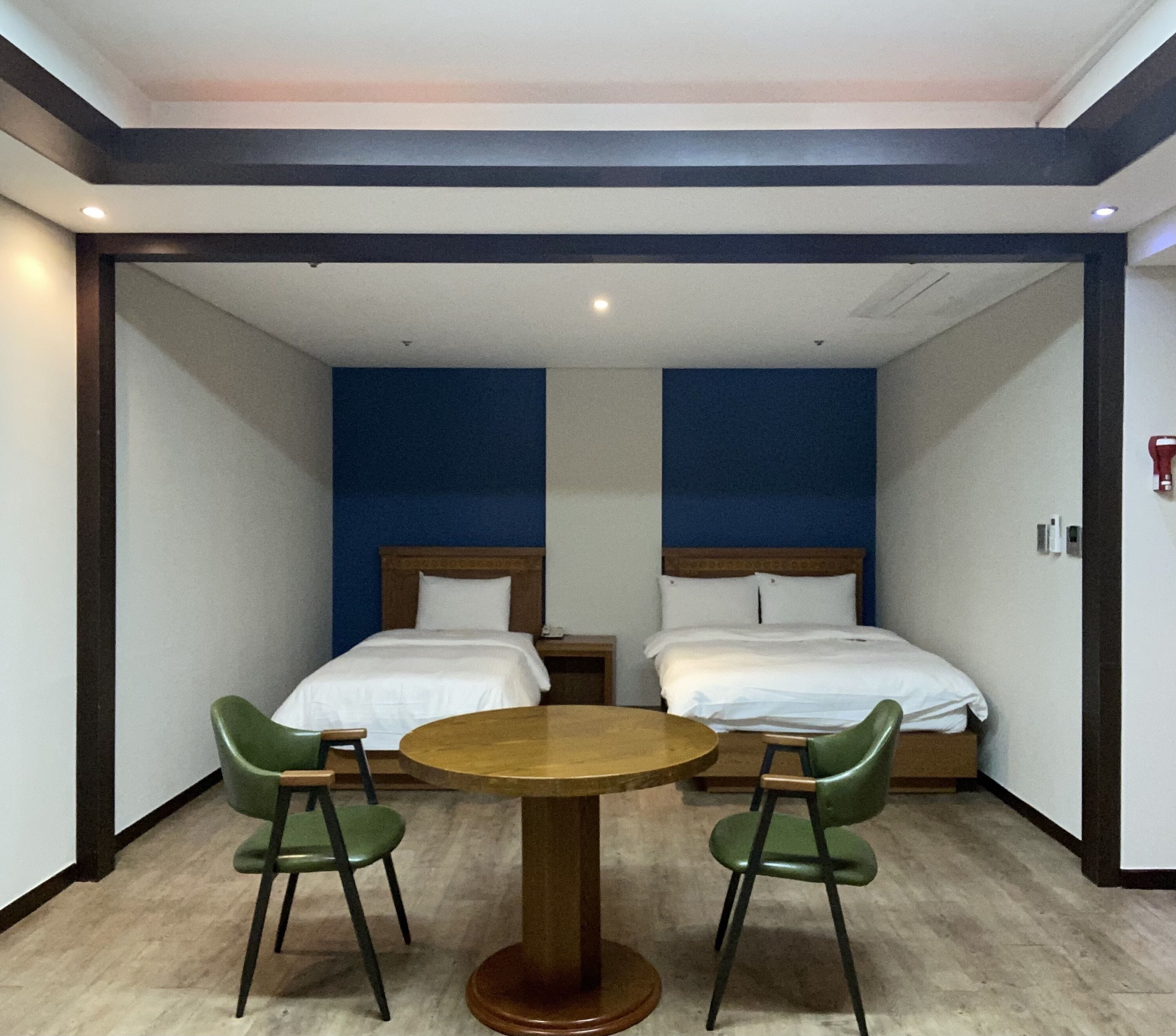 Une chambre d’hôtel avec deux lits, une table ronde et deux chaises vertes.