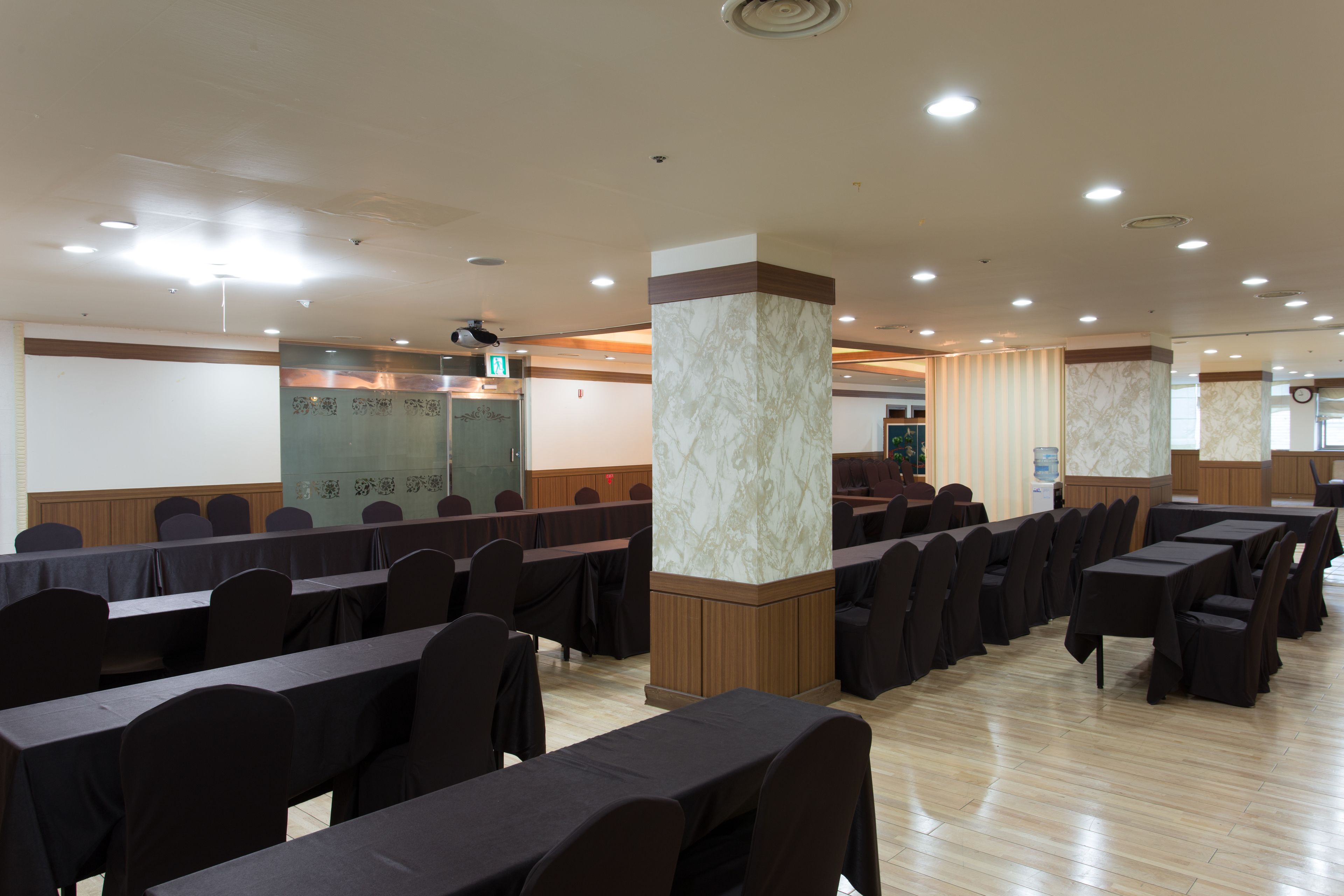 Un salón de conferencias con filas de mesas y sillas, un pilar de mármol y un panel de pared de madera.